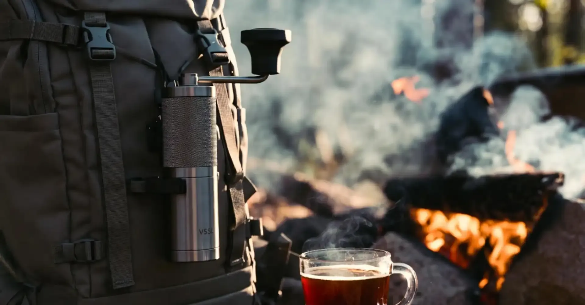 The VSSL Java manual grinder clipped to a backpack in a rugged outdoor camping setting.